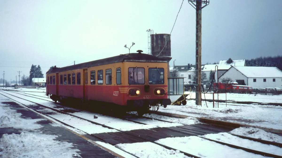 Autorail rouge et jaune sur une voie enneigée à Bertrix